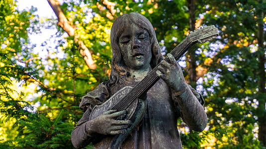 gray concrete person playing guitar sculpture near green leafed tree thumbnail