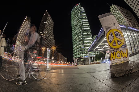 Man Riding Bicycle on Sidewalk Near Buildings during Nighttime thumbnail