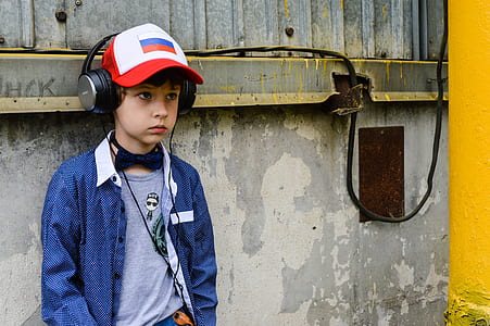 boy leaning on concrete wall while using headphones thumbnail