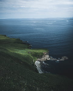 green grass field mountain beside sea under cloudy sky thumbnail