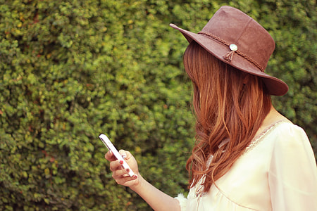 close up photo of person wearing brown hat and white shirt holding smartphone thumbnail