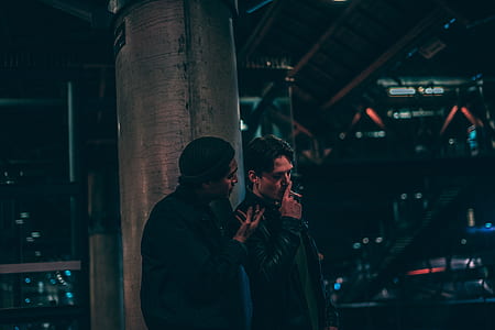 two men standing talking near metal post at night time thumbnail