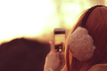 selective focus photography of woman wearing earmuffs taking camera thumbnail