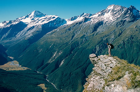 person standing on ledge overlooking mountain ranges thumbnail