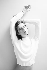 grayscale photo of a woman wearing sweater raising both hands leaning on wall thumbnail