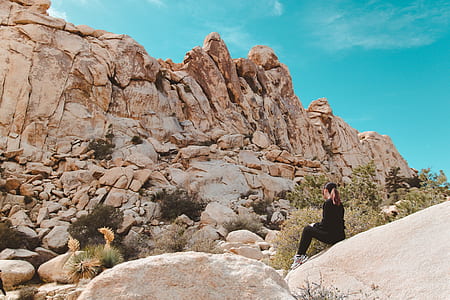woman sitting on boulder in front on brown stone mountain thumbnail