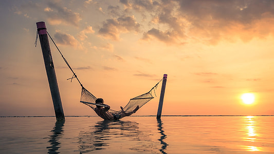 man lying in hammock above body of water during sunset thumbnail