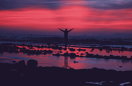 person standing on seashore while raising hands during sunset thumbnail