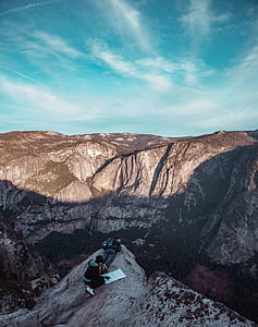 person kneeling beside man lying on edge of top of mountain thumbnail