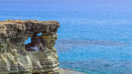 couple sitting on a cliff cave near ocean at daytime thumbnail