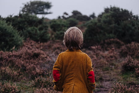 boy in brown suit facing bush plants thumbnail