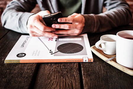 person holding Android smartphone beside two white ceramic mugs thumbnail