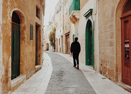 person walking on alley between concrete building during daytime thumbnail
