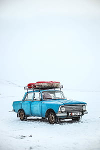 blue sedan with two rafts on roof parked on snow covered surface thumbnail