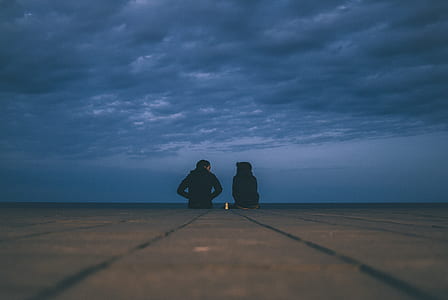 silhouette of two person sitting on ground under gloomy skies thumbnail