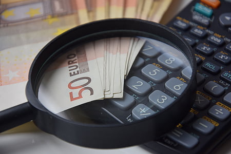 magnifying glass on top of black desk calculator and 50 Euro banknotes thumbnail