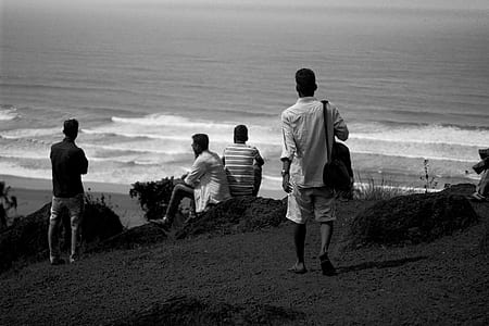 grayscale photo of people on hill near body of water thumbnail