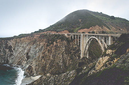photo of arch-shaped concrete bridge near body of water thumbnail