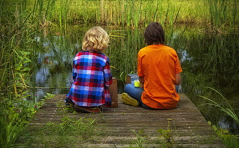 two men on brown wooden dock in front of body of water with grasses thumbnail