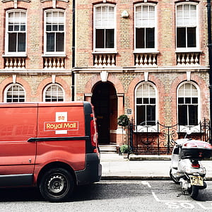 Red Royal Mail Parked Near Brown Brick Building thumbnail