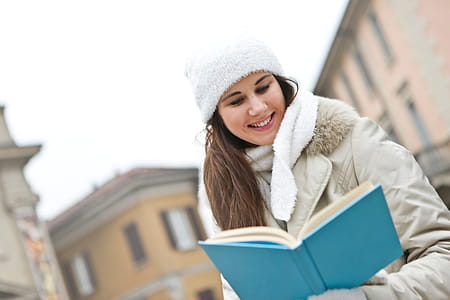 A young causasian woman wearing a jacket reading a book outdoors in winter season thumbnail