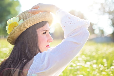woman wearing white long-sleeved blouse holding her brown hat with yellow flower thumbnail