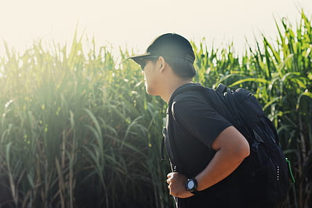 man wearing backpack and cap standing near grasses thumbnail
