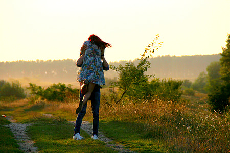 man carrying woman in white floral dress on green grass field photography thumbnail