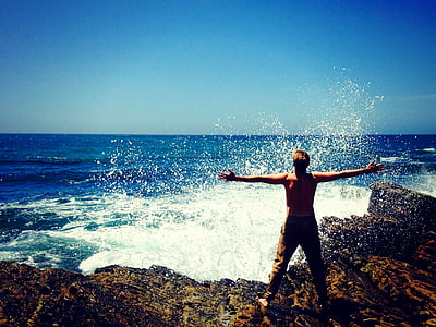 person standing on black rocks beside a body of water thumbnail