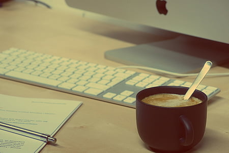 black filled cup beside white Apple keyboard on brown surface thumbnail