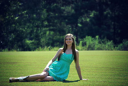 smiling woman wearing seafoam-green strapless dress sitting on grass field during daytime thumbnail