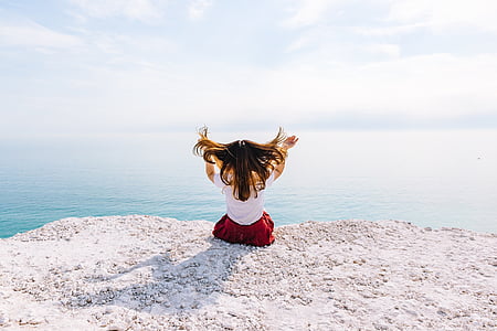 woman sitting on cliff near body of water during daytime thumbnail