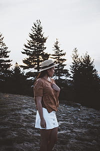 woman wearing beige hat, brown scoop-neck short-sleeved shirt, and white skirt standing on rock formation thumbnail