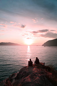 two person's sitting on cliff in front of sea thumbnail