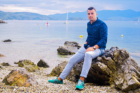 man in blue dress shirt sitting on coastal rock during daytime thumbnail
