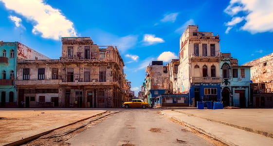 yellow sedan parks near white and beige concrete buildings at daytime thumbnail
