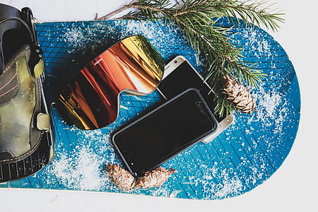 high angle photo of snow goggles and two turned off smartphones with pine cones thumbnail
