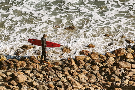 man holding red surfboard walking on seashore thumbnail