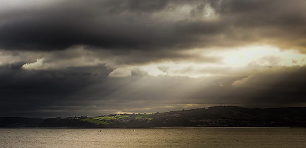 landscape photography of body of water near mountain during crepuscular rays thumbnail
