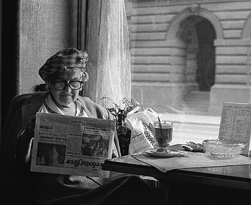 grayscale photo of woman sitting on chair while reading newspaper thumbnail