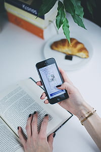 person holding black iPhone 5 while reading book thumbnail