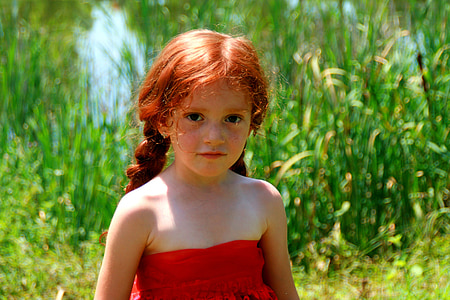 girl in red strapless dress standing near green grass during daytime thumbnail