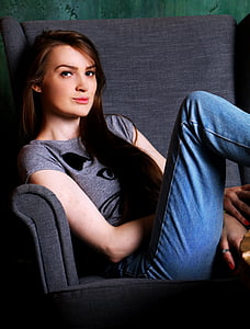 woman wearing gray shirt and blue denim jeans sitting on gray sofa chair thumbnail