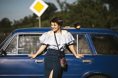 Woman Wearing White Off-shoulder Top While Touching Blue Car thumbnail