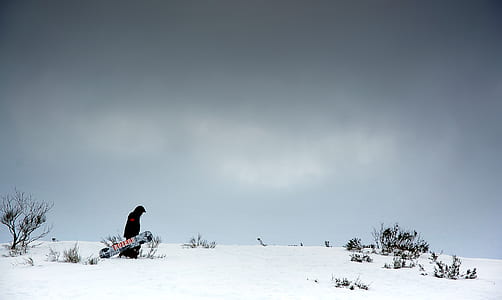 person holding snowboard walking on snow covered road thumbnail