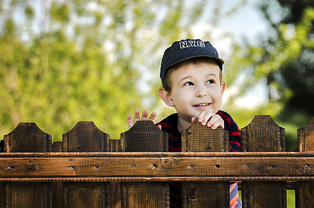 boy wearing black cap standing behind wooden fence thumbnail