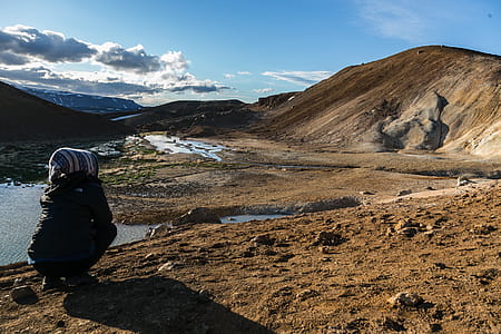 Person Squatting Front of Brown Mountain thumbnail