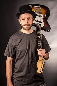 man wearing black crew-neck t-shirt and hat holding sunburst electric guitar thumbnail