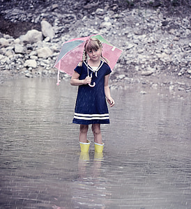 girl standing in the river holding multicolored umbrella while pouring rain thumbnail