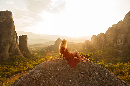 woman wearing red dress sitting on rock formation at daytime thumbnail